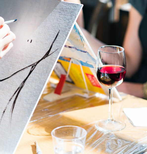 a glass of wine sitting next to a painters canvas