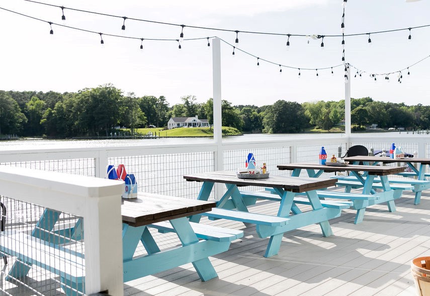 an outdoor patio with string lights and light blue picnic tables looking out of the water
